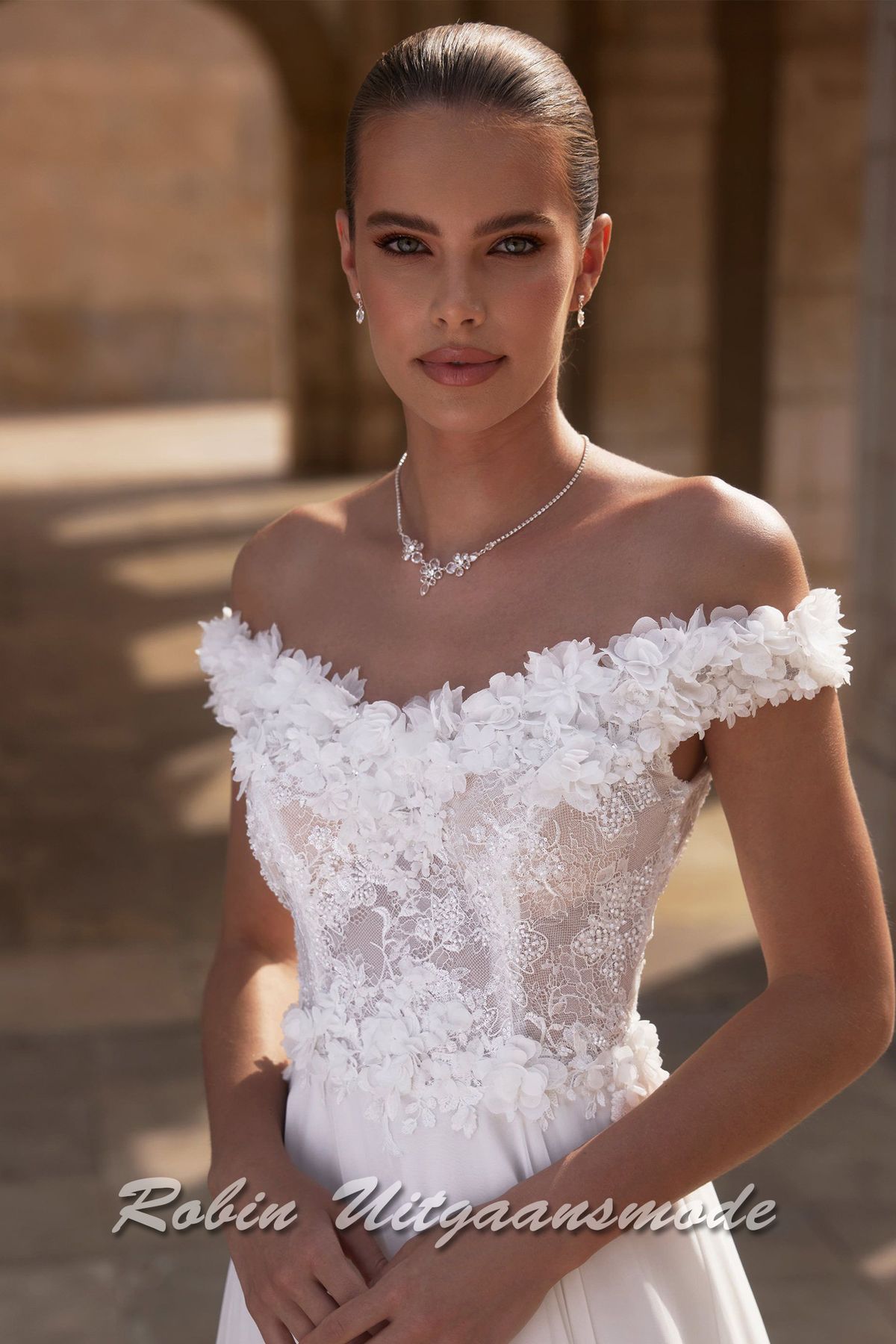 Close-up van de Off-shoulder trouwjurk met kanten lijfje,  een bloemen versierde halslijn, sluikvallende chiffon rok met semi lange sleep