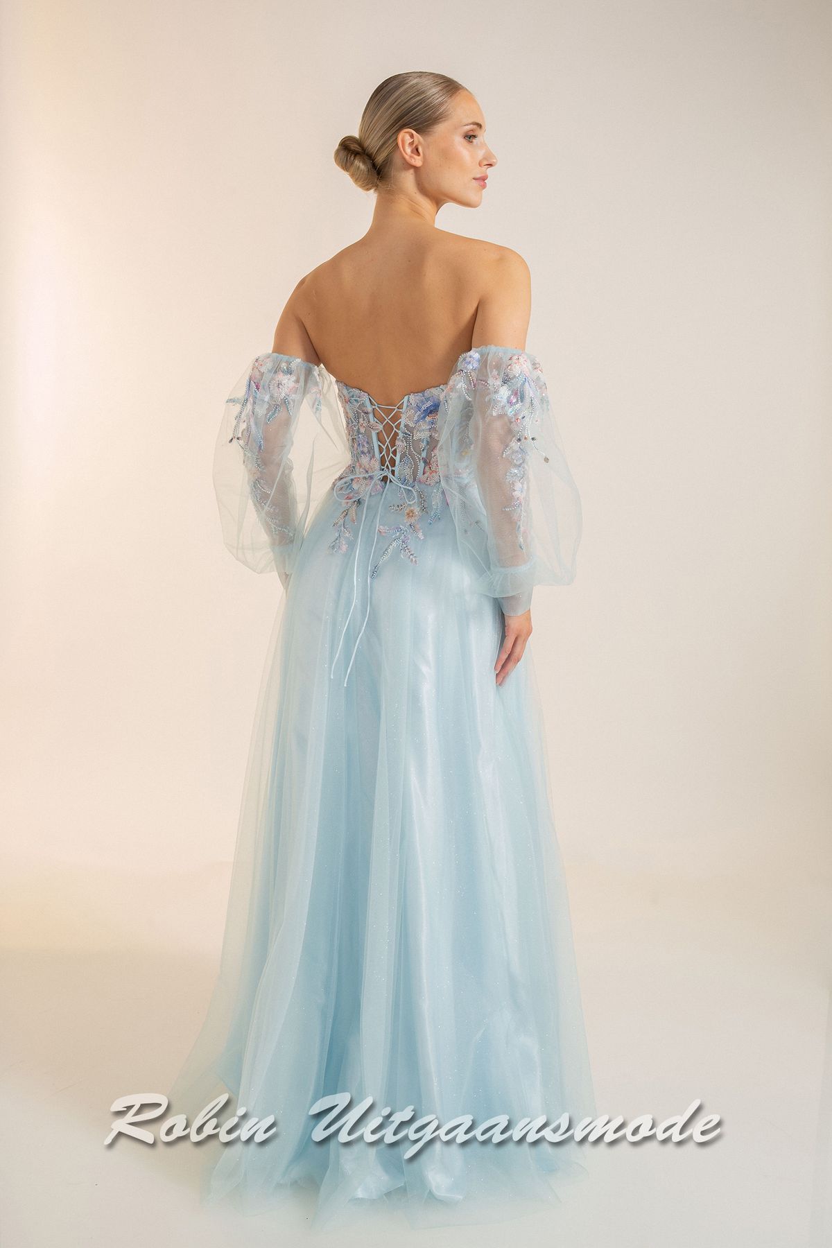 Achterkant van de Strapless lichtblauwe galajurk met bloemen lijfje, losse pofmouwen van tule en springerige rok van soft tule