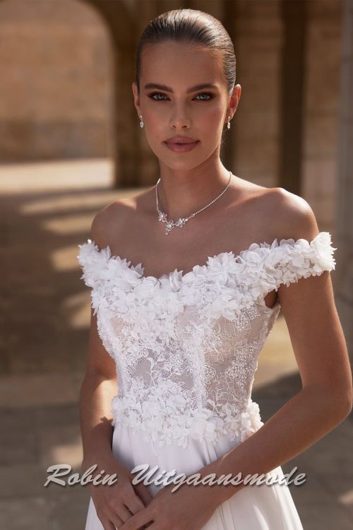Close-up van de Off-shoulder trouwjurk met kanten lijfje,  een bloemen versierde halslijn, sluikvallende chiffon rok met semi lange sleep