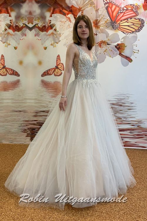 Zijaanzicht van de Ivoorkleurige glamour trouwjurk met kralen versierd lijfje, een illusie diep V-hals, brede schouderbanden, blote schouders en A-lijn glittertule rok
